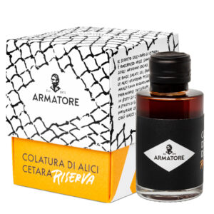 ARM152615 Kleine Flasche Colatura di Alici Riserva von Armatore neben schwarz-weiss bedruckter Geschenkbox.