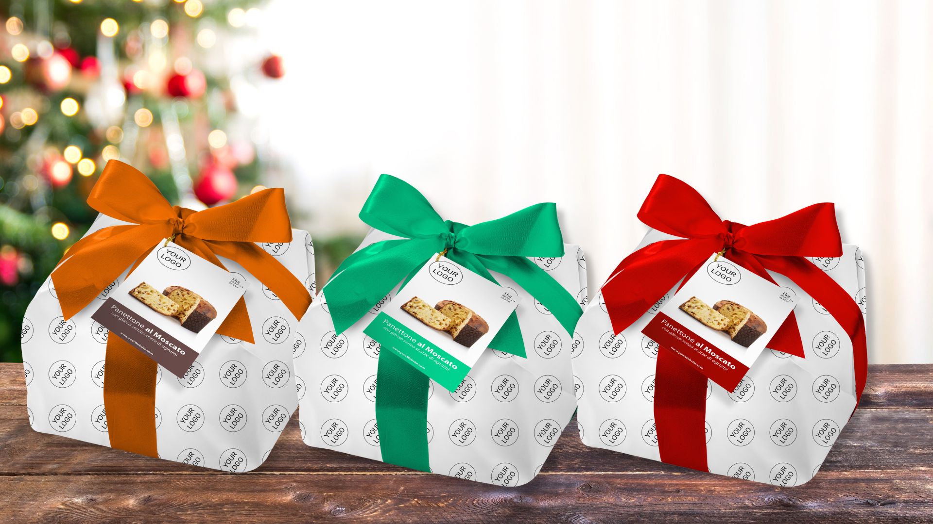 Drei weiss verpackte Panettone mit orangen, grünen und roten Geschenkschleifen vor einem unscharfen Weihnachtsbaum.