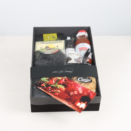 Schwarze Geschenkbox mit Feinkostprodukten wie Tomatensauce, Teigwaren, Gewürz, Öl und einer roten Weihnachts-Grusskarte.