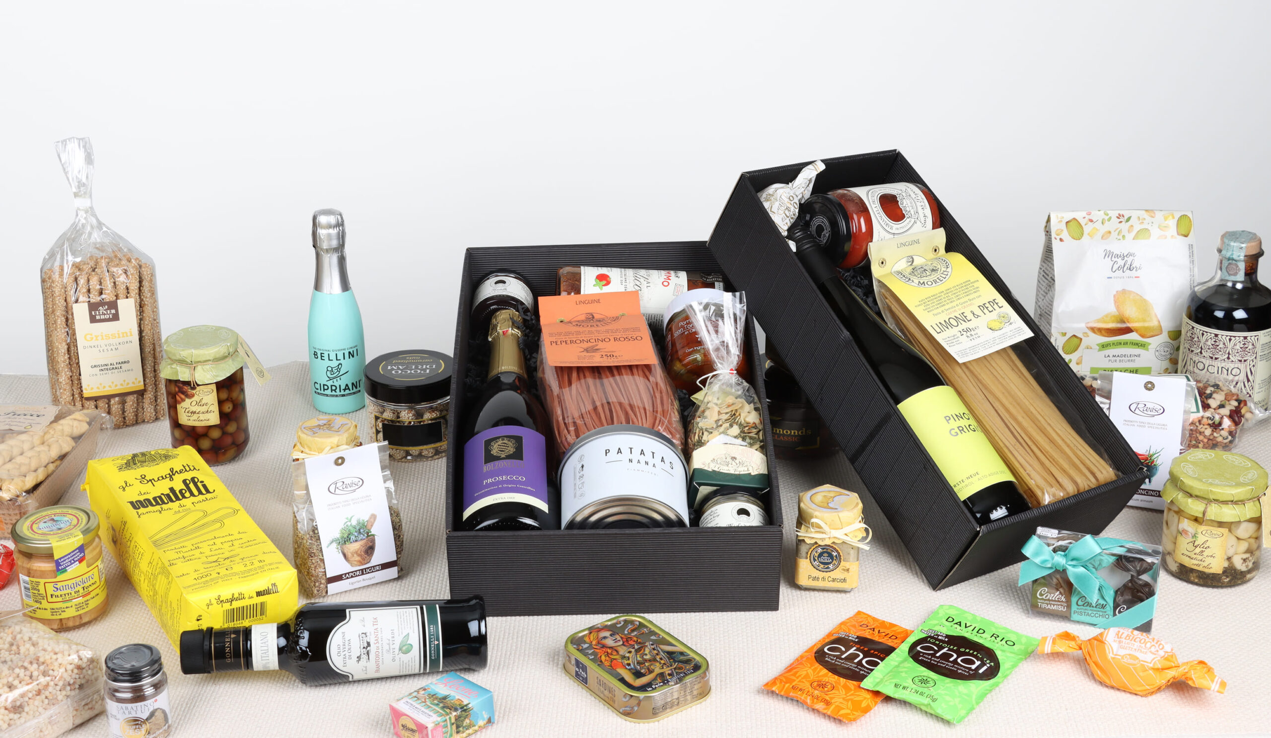 Zwei schwarze Geschenkkörbe gefüllt mit Weinfiaschen, Teigwaren, Oliven und italienischen Spezialitäten auf hellem Grund.